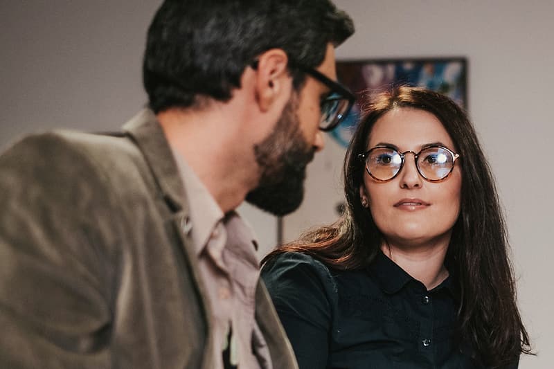 Doi colegi care discută la masa de lucru, cu documente și o cană de cafea