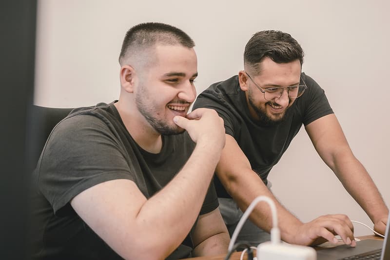 Doi colegi dintr-o echipă mică, amuzați de ceva pe ecranul laptopului